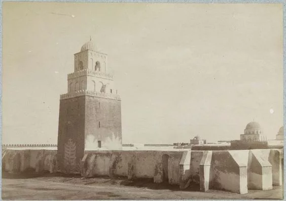 Photographie ancienne de la Grande Mosquée de Kairouan en Tunisie, montrant son architecture islamique traditionnelle avec un minaret carré et des coupoles, fondée par Uqba Ibn Nafi au 7ᵉ siècle.