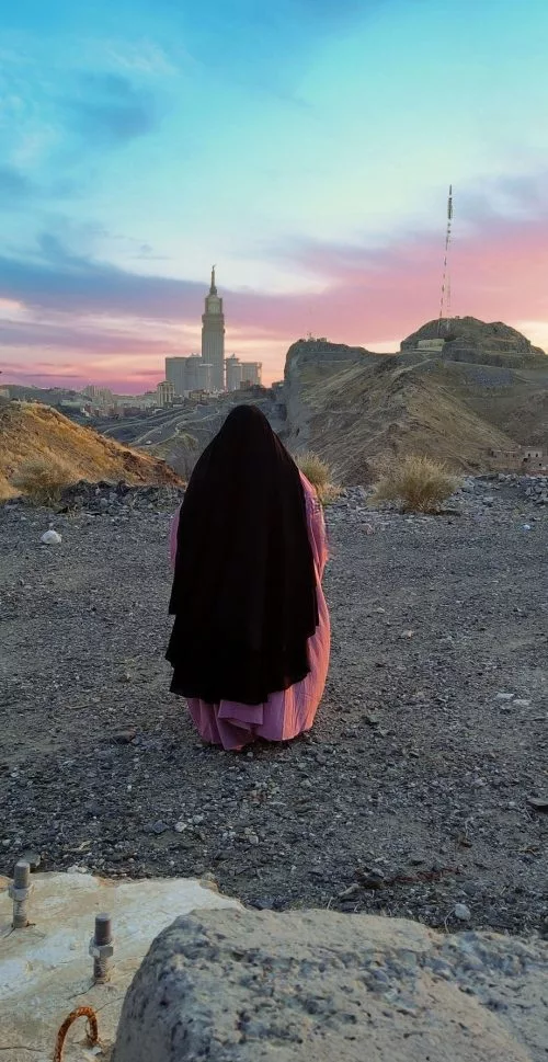 femme que l'on voit de dos avec son jilbab en haut d'une montagne, en face de la kaaba