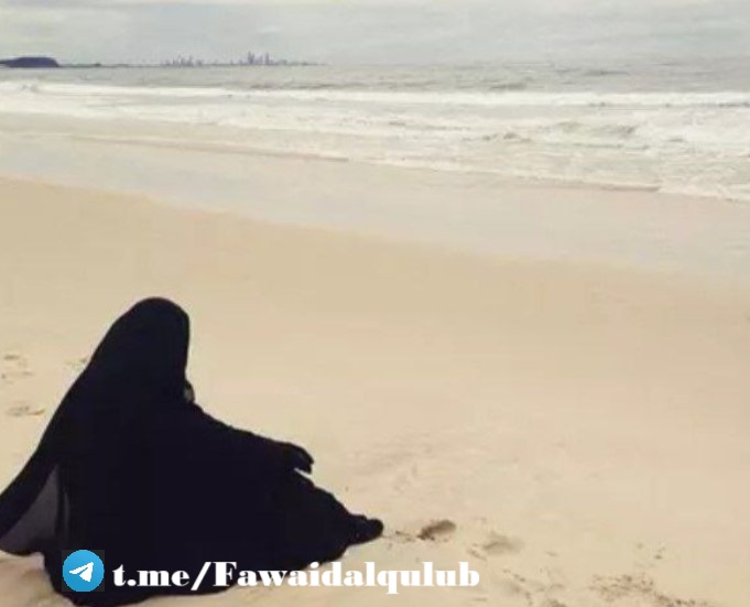 Une personne en vêtements noirs est assise sur une plage, regardant vers l'océan. L'atmosphère est calme et contemplative, avec des vagues qui viennent doucement lécher le rivage.
