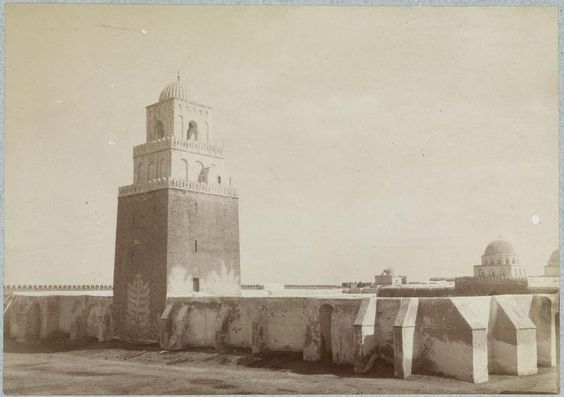 Photographie ancienne de la Grande Mosquée de Kairouan en Tunisie, montrant son architecture islamique traditionnelle avec un minaret carré et des coupoles, fondée par Uqba Ibn Nafi au 7ᵉ siècle.