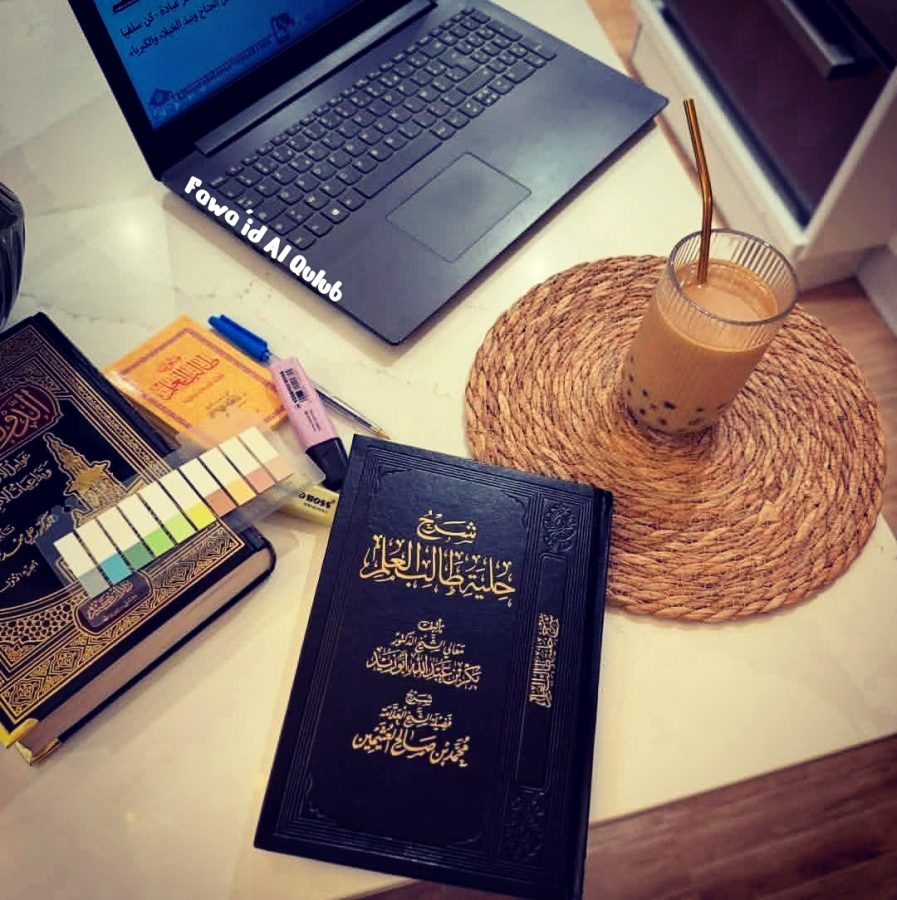 Bureau d’étude avec un ordinateur portable allumé sur une page en arabe, des livres islamiques, une boisson au café, des stylos, surligneurs et étiquettes colorées.