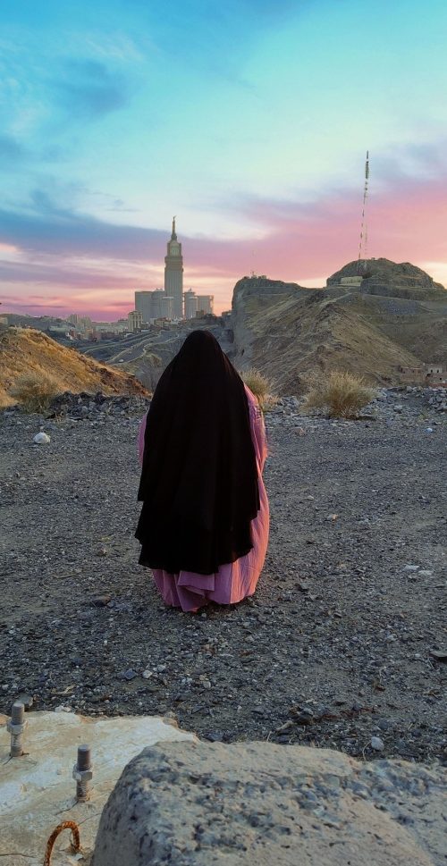femme que l'on voit de dos avec son jilbab en haut d'une montagne, en face de la kaaba